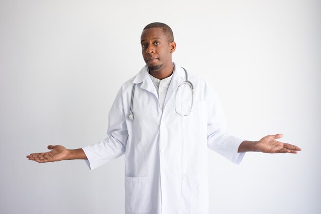 Serious black male doctor holding empty space with both hands.