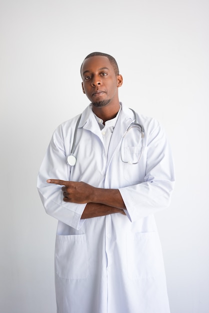 Serious black male doctor pointing aside. Medical service advertising concept.