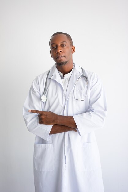 옆으로 가리키는 심각한 흑인 남성 의사. 의료 서비스 광고 개념입니다.