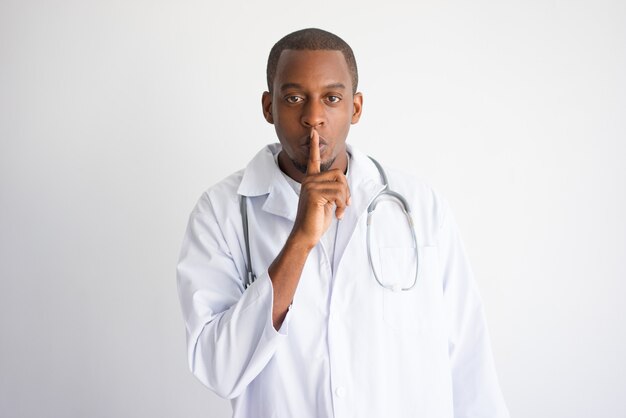 深刻な黒人男性の医師は、沈黙のジェスチャーを示しています。