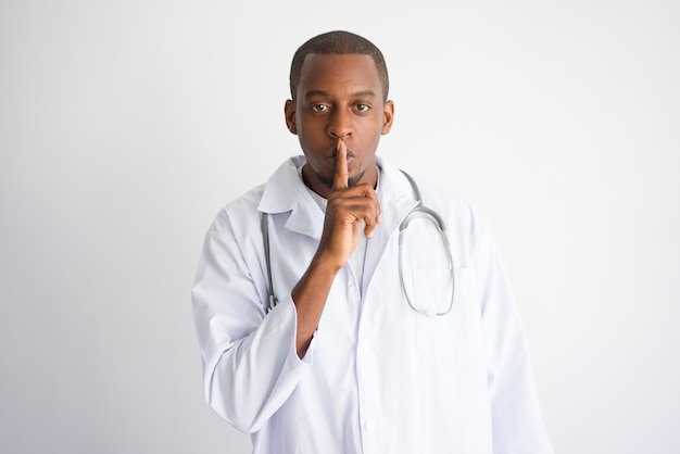Серьезный черный мужской врач показывает молчание жест.