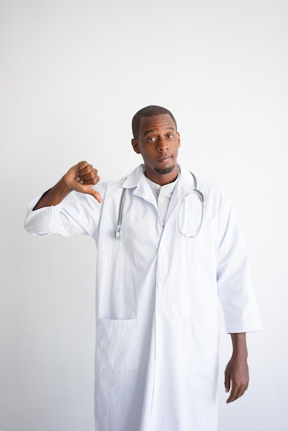 Serious black male doctor showing thumb down. Harm to health concept. 