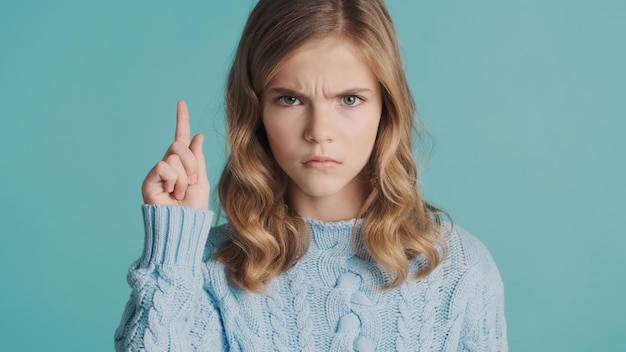 파란색 배경 위에 검지 손가락을 들고 공격적으로 보이는 심각한 금발 10대 소녀 침묵 제스처 화난 소녀