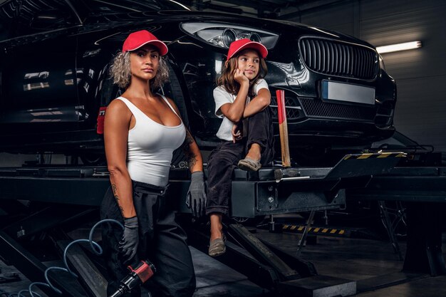 Serious blond woman auto mechanic and her young colleague are posing for photographer.