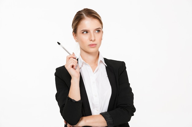 Serious blonde business woman holding pen and looking away over white wall