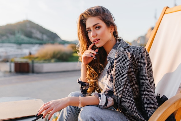 Serious blue-eyed lady chilling in outdoor restaurant on mountain background