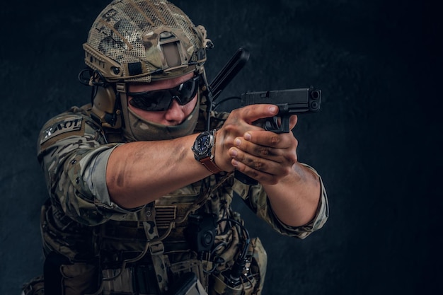 Serious brave soldier in military uniform and sunglasses is aiming with his gun.