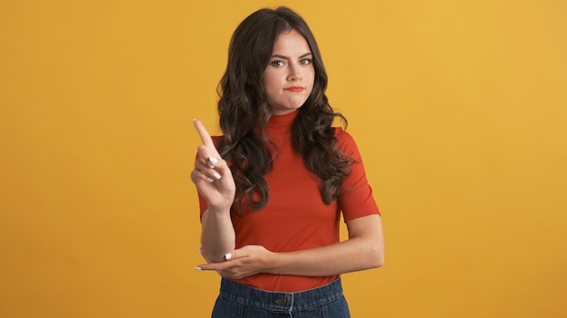 Serious brunette girl in red top confidently showing no gesture on camera over colorful background No expression