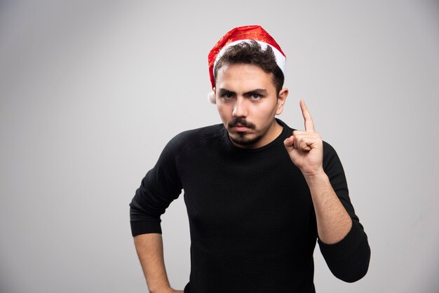 A serious brunette man in Santa's hat showing a finger up and posing