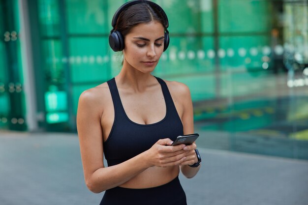 Серьезная брюнетка-спортсменка, одетая в короткие текстовые сообщения, слушает звуковую дорожку в наушниках, размывает фитнес-тренировку
