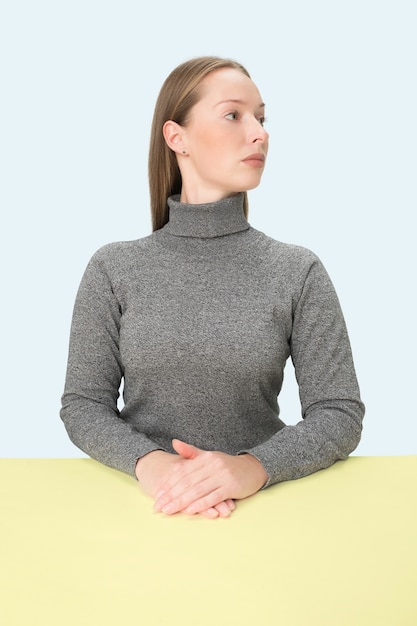 Serious business woman sitting at table over blue  space