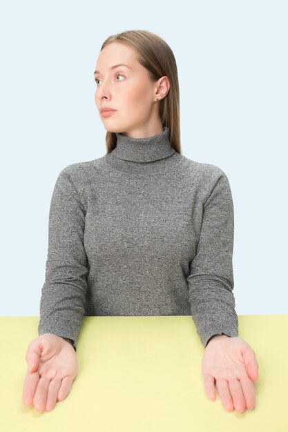 Serious business woman sitting at table over blue  space