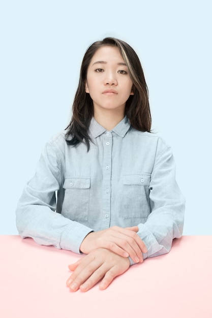 Serious business woman sitting at table, looking at camera isolated on trendy blue studio.