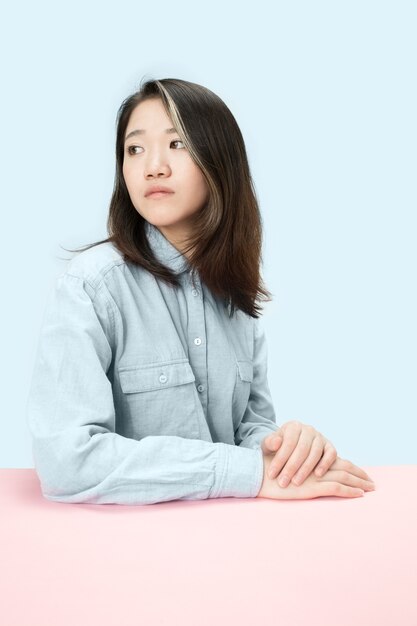 테이블에 앉아 심각한 비즈니스 여자 왼쪽 유행 블루 스튜디오 배경에 고립보고. 아름답고 젊은 얼굴. 여성 절반 길이 초상화.