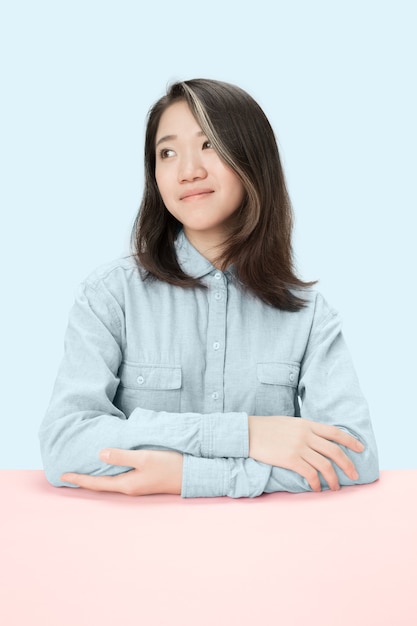 Serious business woman sitting at table, looking at left isolated on trendy blue studio background. Beautiful, young face.