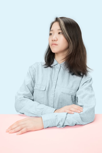 Serious business woman sitting at table, looking at left isolated on trendy blue studio.