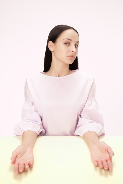 Serious business woman sitting at table on a pink  space