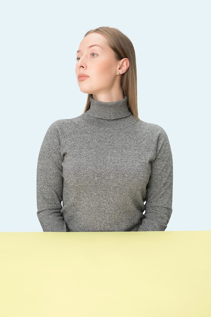 Serious business woman sitting at table on a pink studio wall