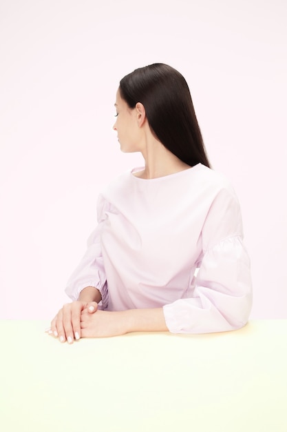 Serious business woman sitting turned away at table on a pink studio wall