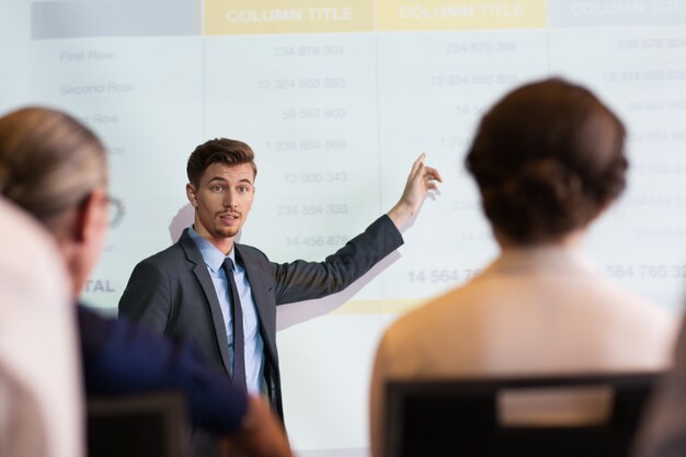 Serious Businessman Explaining Table to Audience