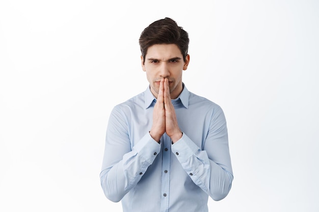 Foto gratuita uomo d'affari serio che prega, aspetta notizie con un gesto di accattonaggio, aspetta o anticipa qualcosa, in piedi su sfondo bianco
