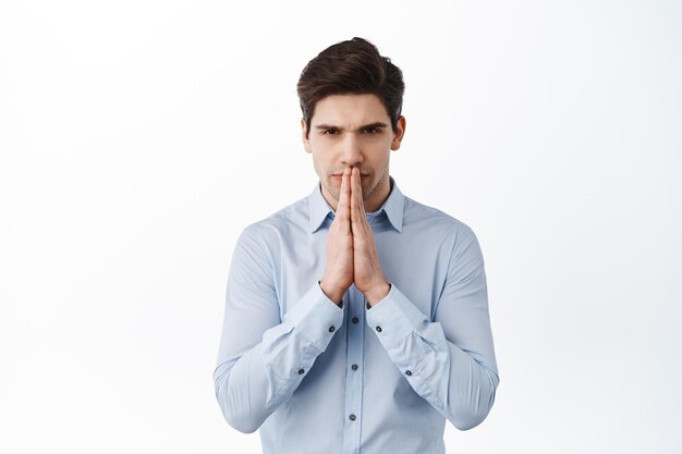 Serious businessman praying, waiting for news with begging gesture, expect or anticipate something, standing over white background