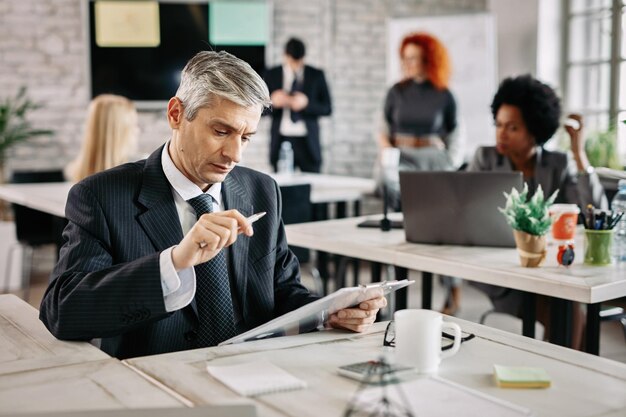 Free Photo serious businessman sitting in the office and reading business reports there are people in the background