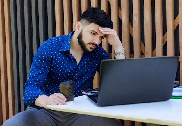 Uomo d'affari serio in camicia maculata che lavora con il computer portatile in remoto