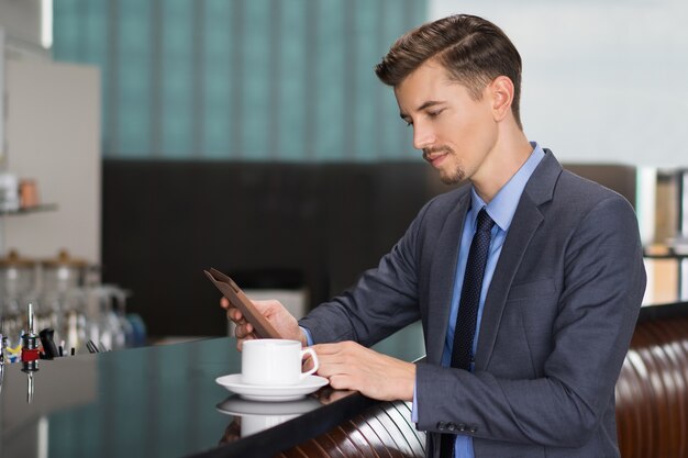 Serious Businessman Using Tablet at Cafe Counter