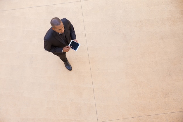 Free photo serious businessman with tablet going through office hall