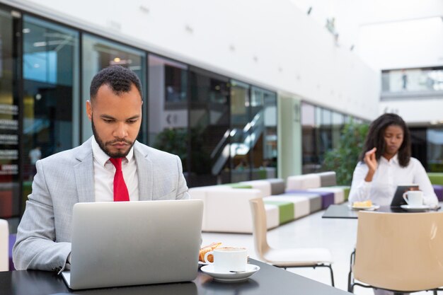 Serious businessman working on laptop while drinking coffee