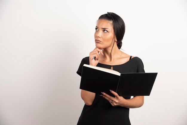 Serious businesswoman with notebook standing on white wall.