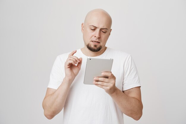 Serious busy bald guy look at digital tablet