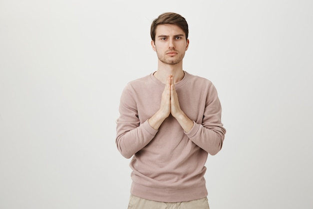 Serious caucasian man pleading, holding hands in pray as supplicating