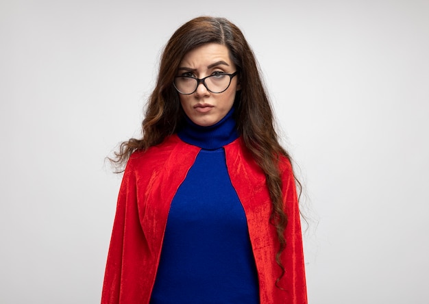 Serious caucasian superhero girl with red cape in optical glasses looks at camera on white