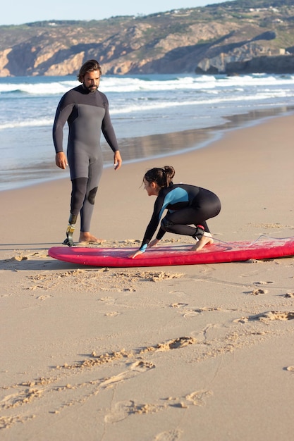기계 다리와 바다 근처 소녀와 함께 심각한 코치. 검은 머리 소녀에게 서핑보드 사용법을 가르치는 중년 남성. 학습, 레저, 활동적인 라이프 스타일 개념