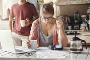 Free photo serious and concentrated young woman in glasses holding mug in one hand and pen in other, focused on paperwork