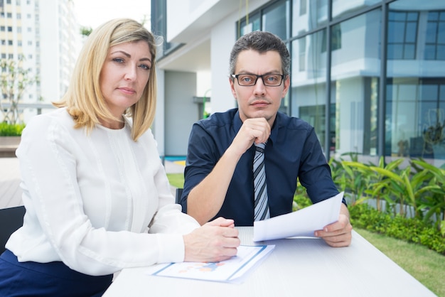 Serious confident business team working with papers and sitting at table outdoors.