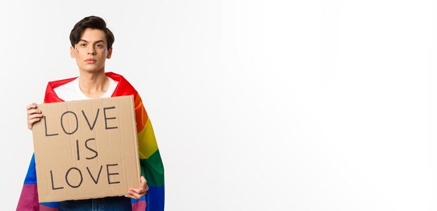 立っているプライドパレードのサインを保持している虹のlgbtの旗を身に着けている深刻で自信のあるゲイの男