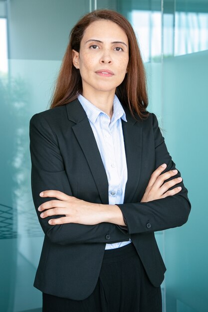 Serious confident red haired business lady wearing jacket, standing with arms folded 
