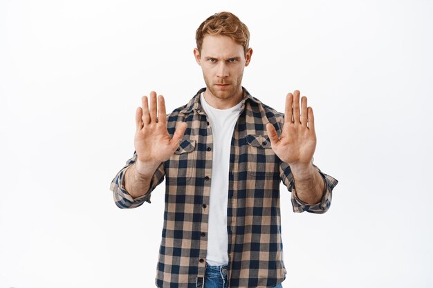 Serious and confident redhead man telling to stop, showing no prohibition gesture, taboo on something, forbid action, look from under forehead determined, blocking and refusing, white background