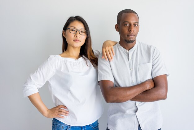 Serious confident young multiethnic couple looking at camera and standing in studio