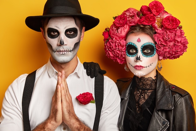 Free photo serious couple zombie keep palms pressed together, dressed in black costume for halloween