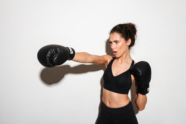 Serious curly brunette fitness woman trains in boxing gloves