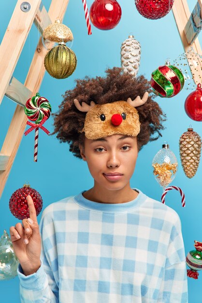 Serious curly woman gets idea how to celebrate New Year raises index finger wears casual domestic clothing poses 