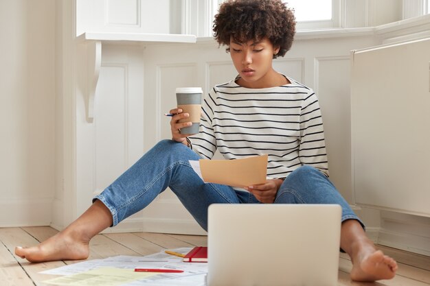 Serious dark skinned female economist thinks on startup project, holds paper document