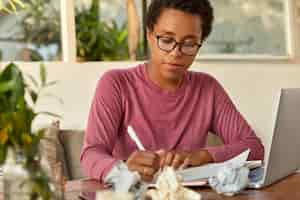 Free photo serious dark skinned woman copywriter writes in sheet of paper