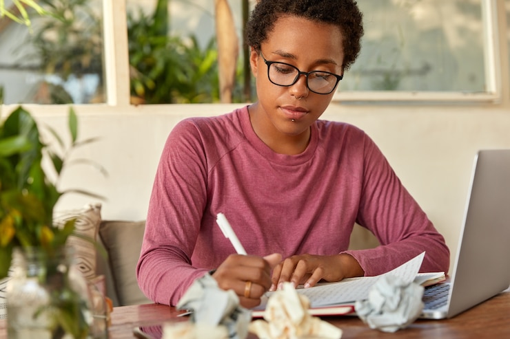 Free Photo serious dark skinned woman copywriter writes in sheet of paper