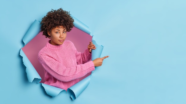 Serious dark skinned woman with curly hair has confident gaze recommends you something