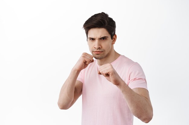 Serious determined man standing in boxing pose, fighting, ready to fight, defending from attack, standing in t-shirt against white background